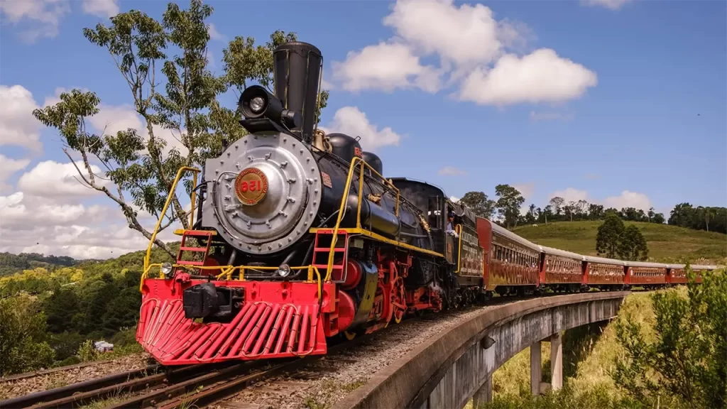 Locomotiva Maria Fumaça atravessando a Serra Gaúcha com paisagens floridas